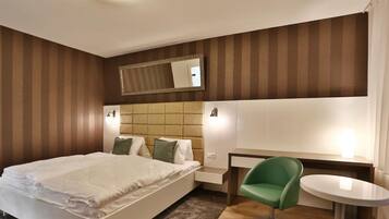 Quarto de hotel moderno com uma cama grande, uma cadeira verde, uma mesa pequena e um espelho na parede.