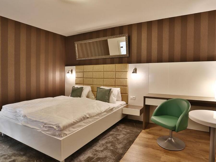 Quarto de hotel moderno com uma cama grande, uma cadeira verde, uma mesa pequena e um espelho na parede.