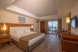 A hotel room with a bed, bedside tables, a desk, a chair, a TV, and a balcony with a view.