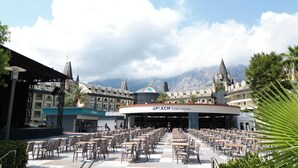 A poolside area with multiple dining tables and chairs, a central building labeled 'SPLASH POOL SNACK,' and a mountainous backdrop. - Crystal Prestige Pearl Collection - All inclusive (Kemer)