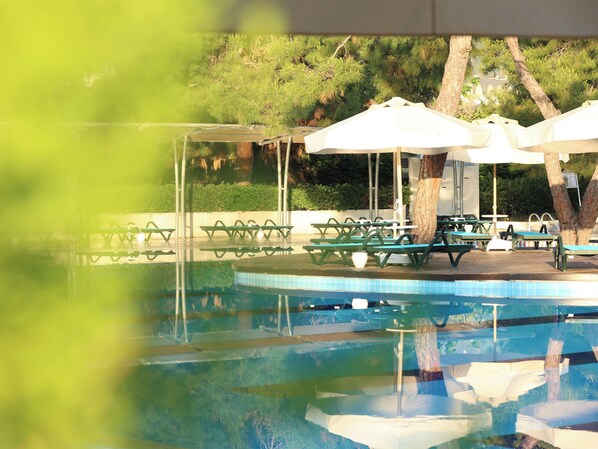 A swimming pool with green picnic tables and white umbrellas, surrounded by trees. - Crystal Prestige Pearl Collection - All inclusive (Kemer)