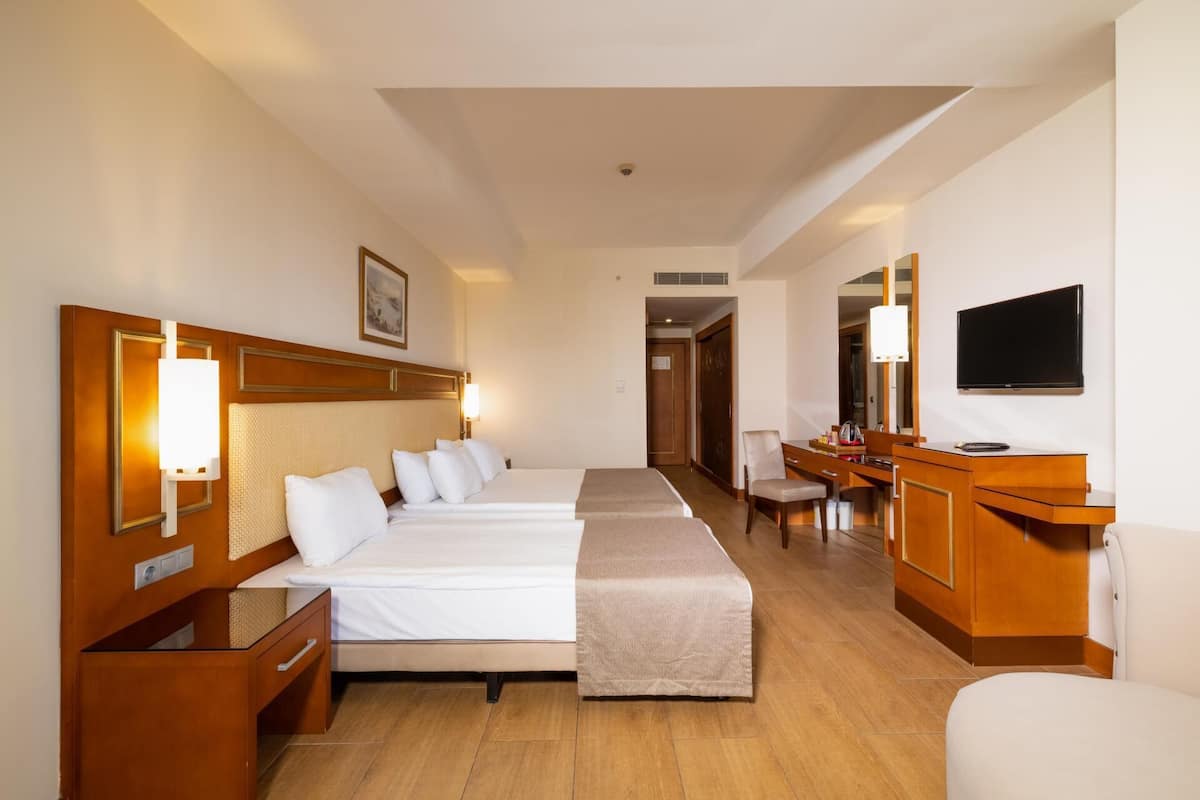 A hotel room with two beds, a desk, a chair, a TV, and a bathroom visible in the background.