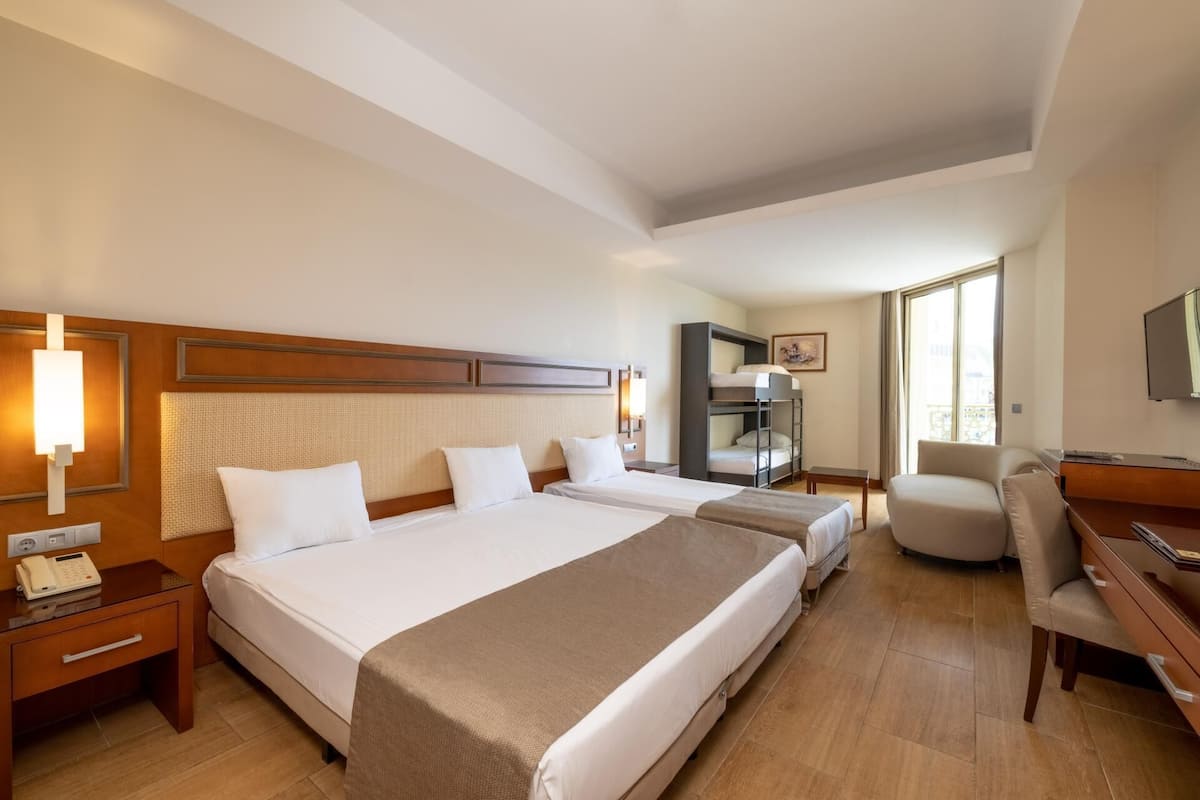 A hotel room with two beds, a desk, a chair, a TV, and a window.