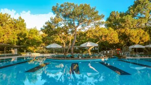 A swimming pool with lounge chairs and umbrellas, surrounded by trees. - Crystal Prestige Pearl Collection - All inclusive (Kemer)