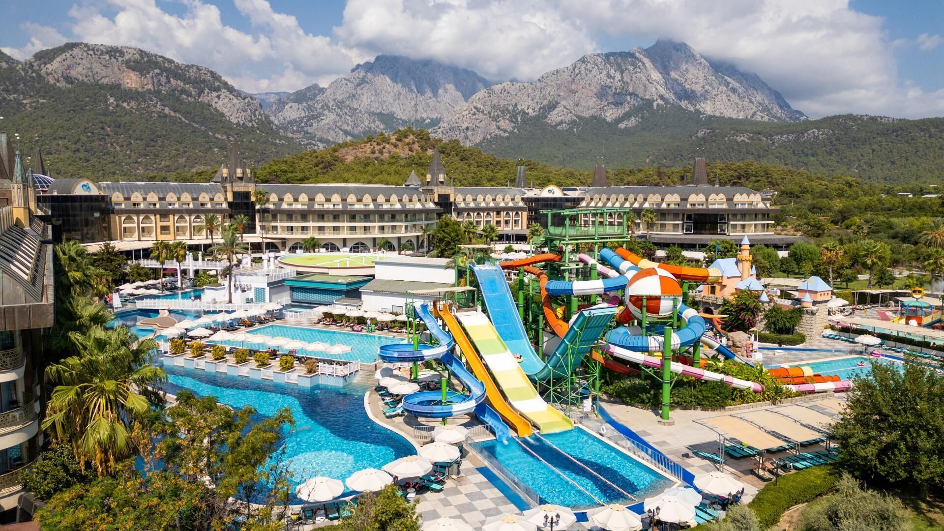 A resort with multiple swimming pools, water slides, and a mountainous backdrop.