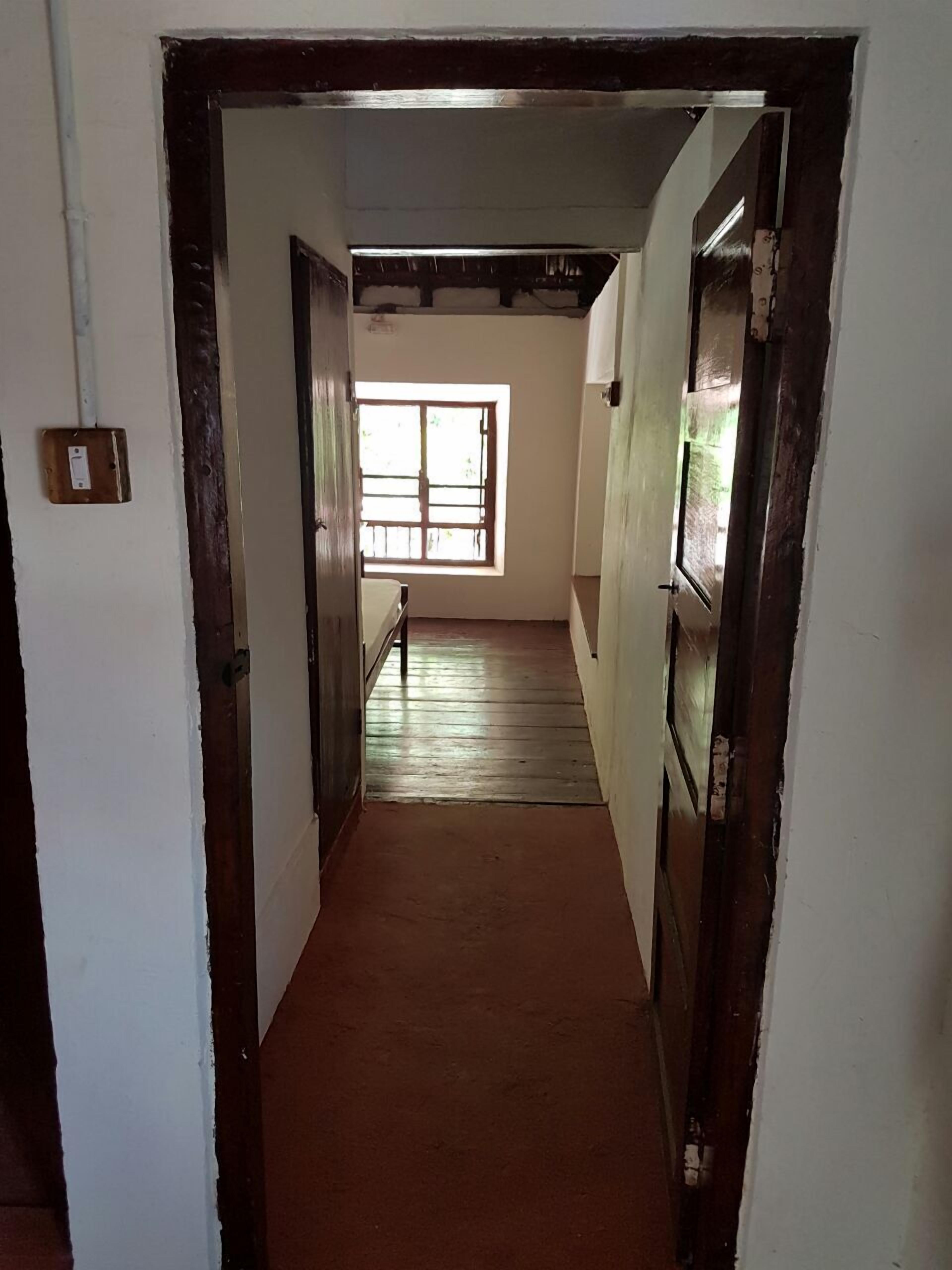 Un couloir étroit doté d’un plancher en bois et de murs blancs. Une fenêtre se trouve au bout du couloir, permettant à la lumière naturelle d’entrer.
