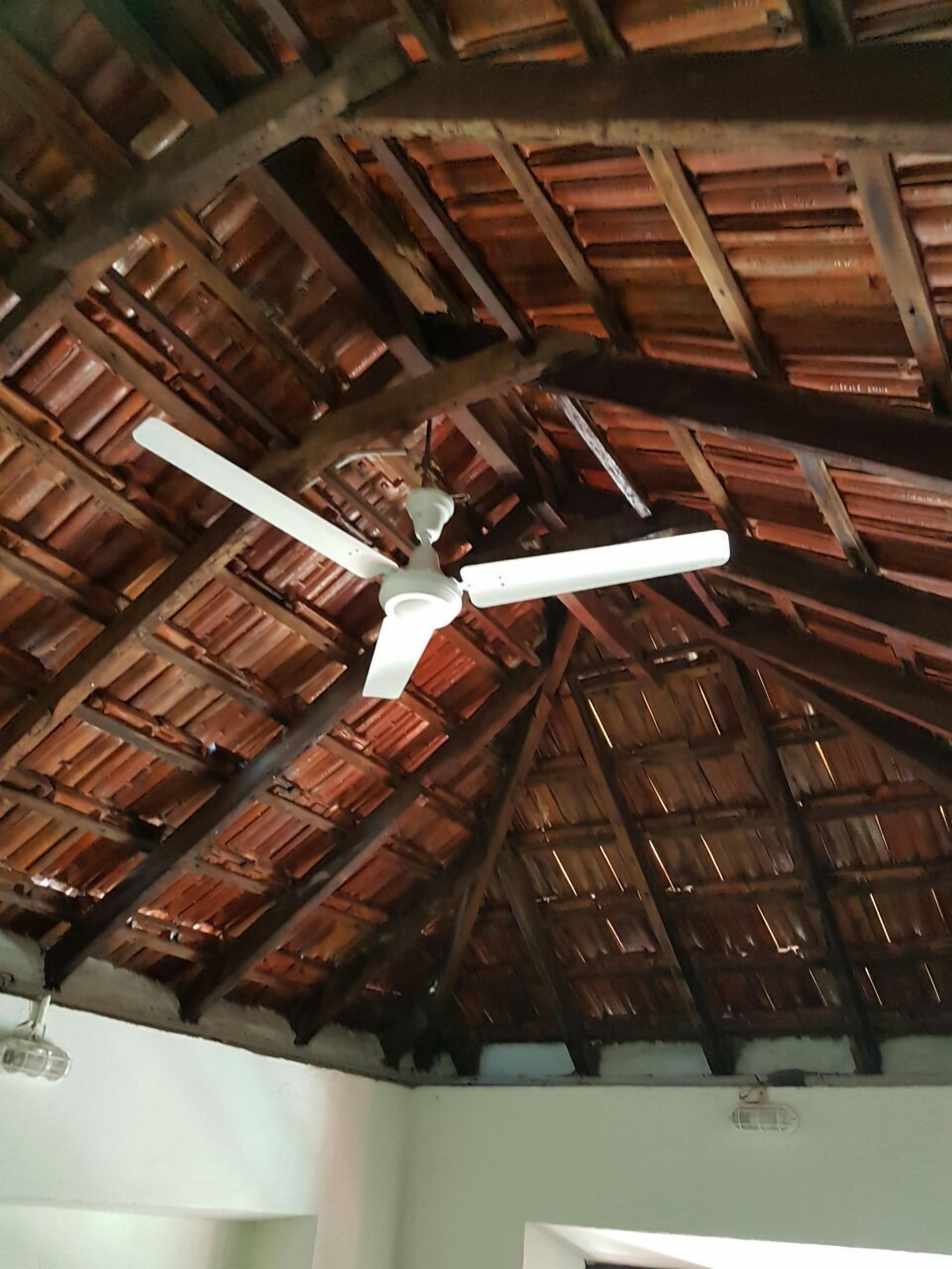 Una habitación con techo inclinado, vigas de madera y un ventilador de techo.