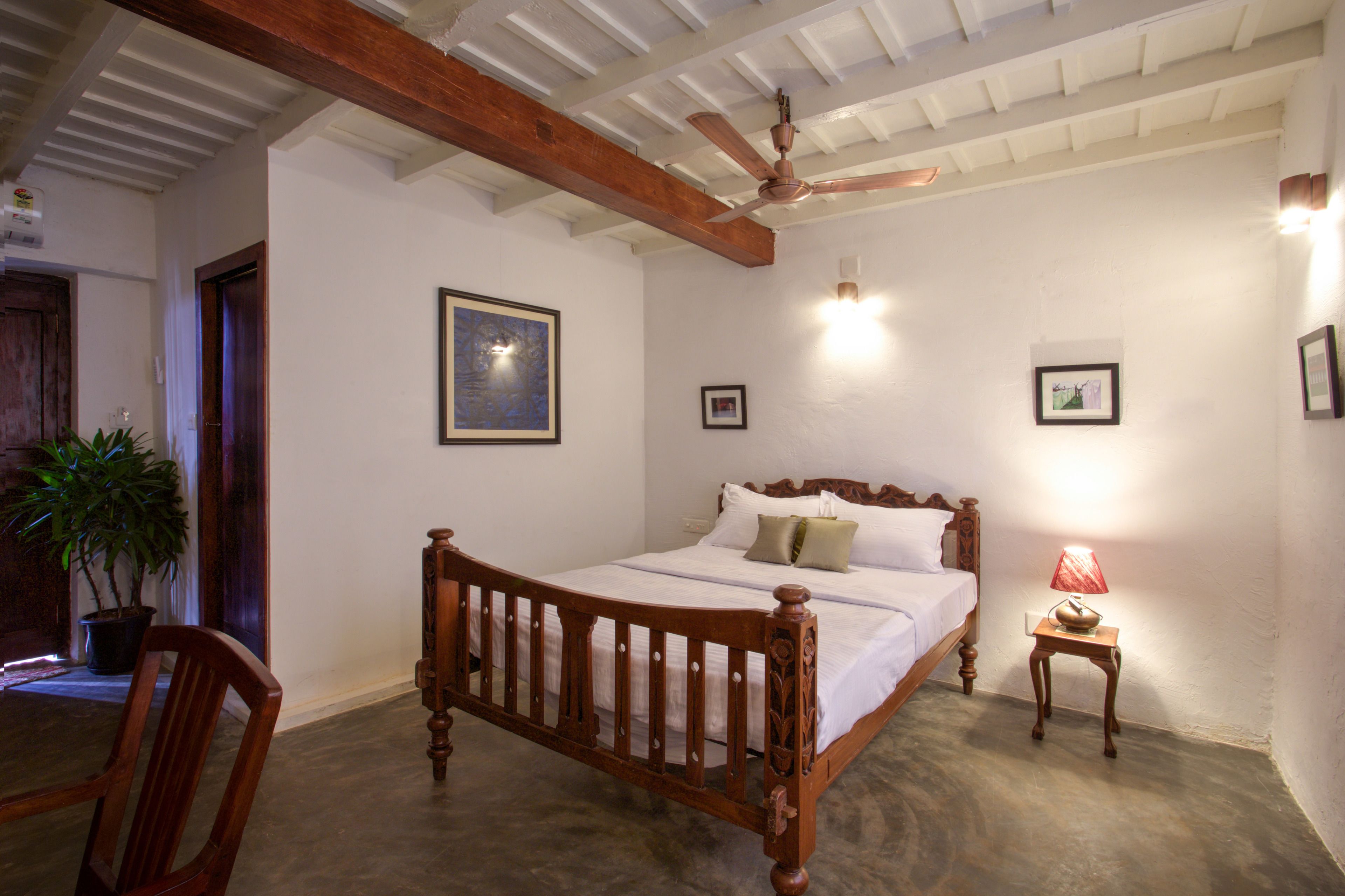 Ein Schlafzimmer mit einem Holzbett, Deckenventilator, Nachttisch mit Lampe und gerahmten Bildern an der Wand.