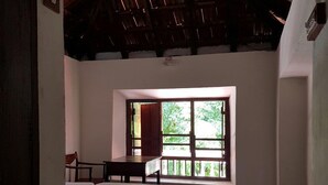 A room with a wooden floor, a bed, a window with a view of greenery, and a thatched roof. - Niyati - Boutique Stay (Kochi)