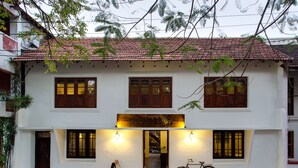 A two-story building with a tiled roof, wooden shutters, and a sign above the entrance. - Niyati - Boutique Stay (Kochi)