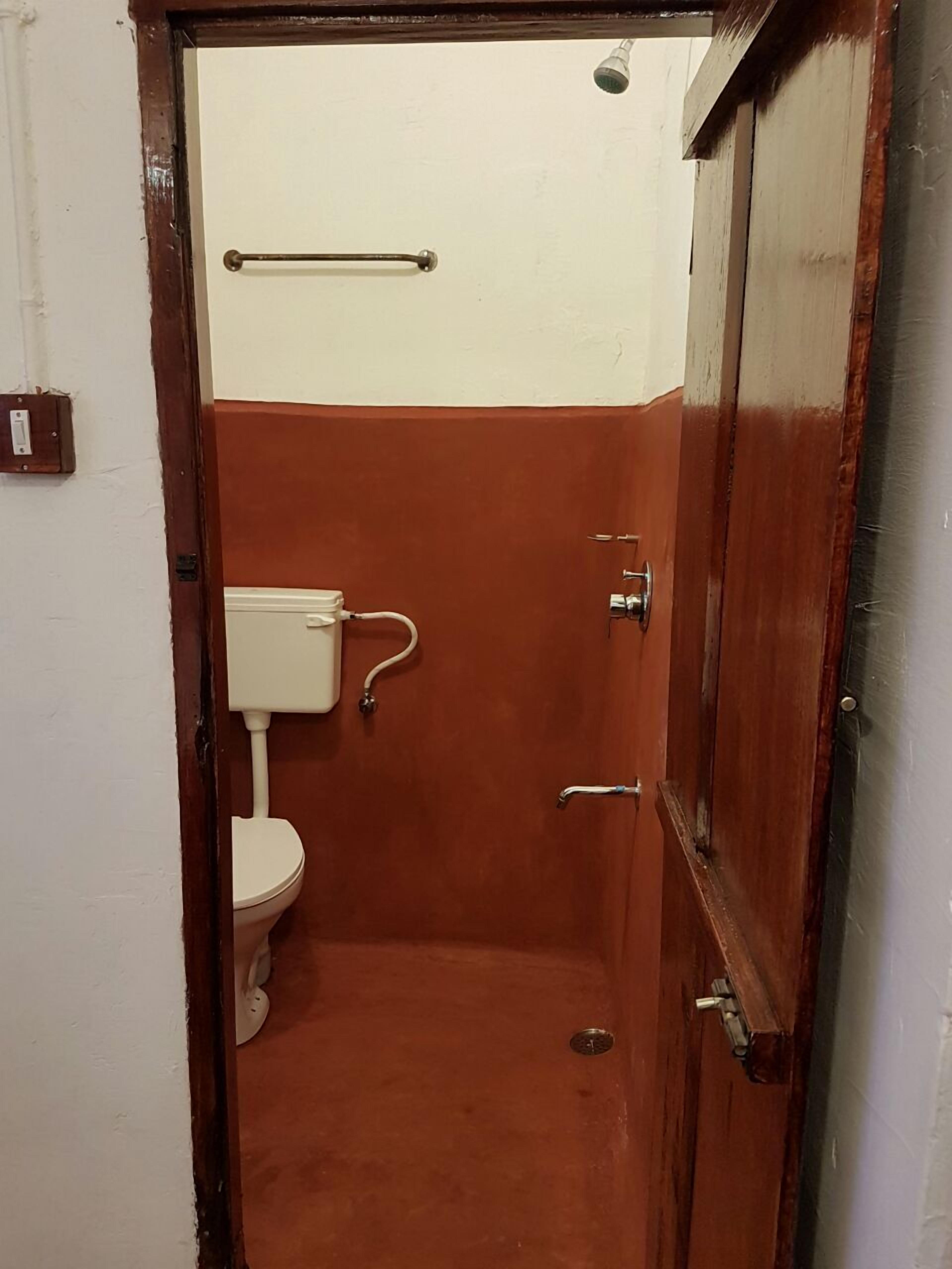 A small, enclosed bathroom with a toilet, a handrail, and a door.