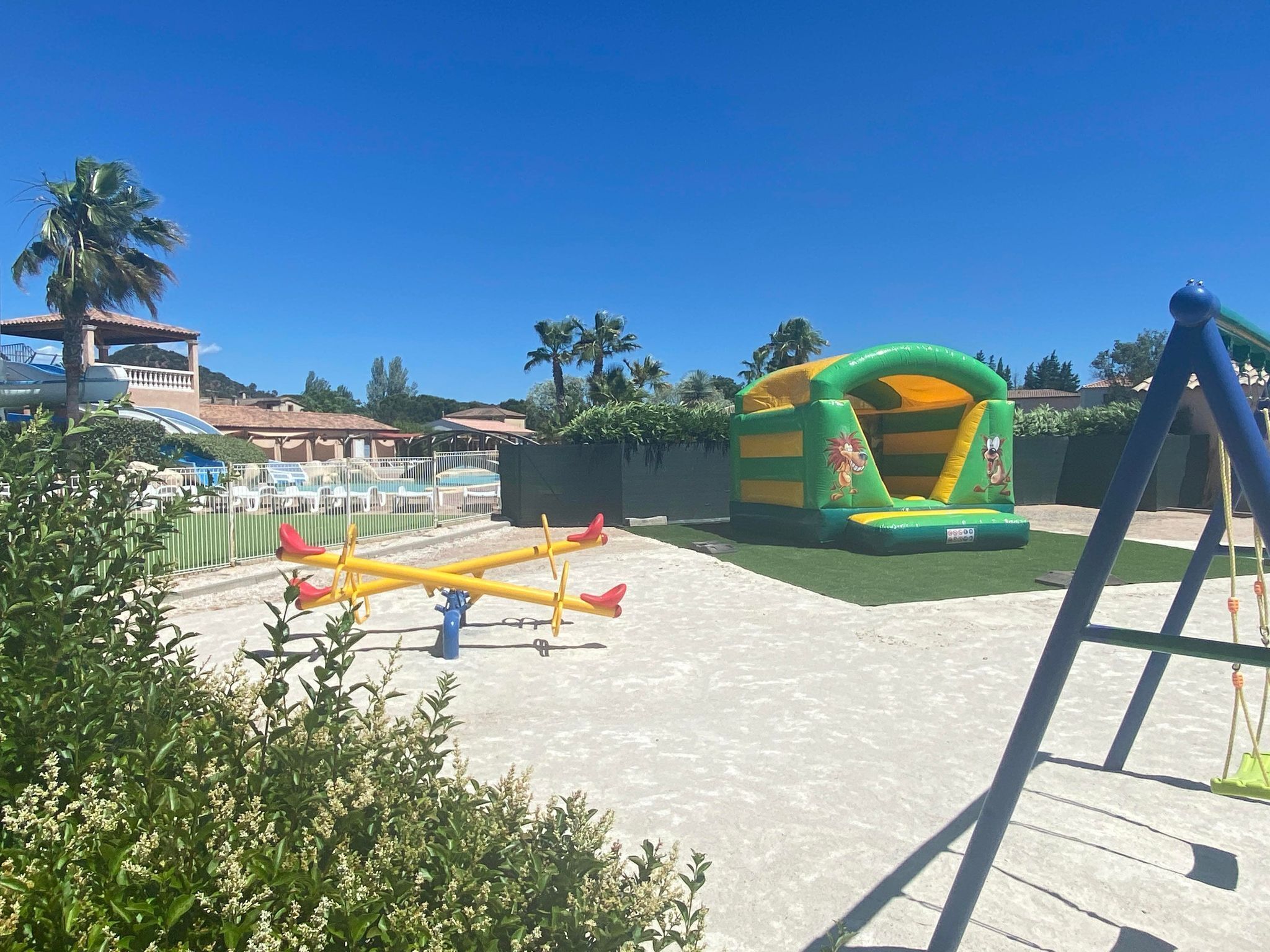 An outdoor playground with a seesaw, a bounce house, and a swing set.