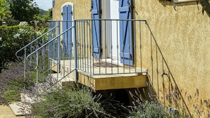 Un bâtiment à deux étages doté d’un balcon, d’un escalier et d’une porte avec des volets bleus.