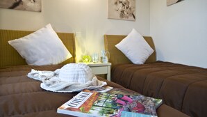 Une chambre d’hôtel avec deux lits, chacun équipé d’un oreiller et d’une couverture. Il y a une table de chevet avec une lampe et une carafe d’eau. Un magazine est posé sur le lit.