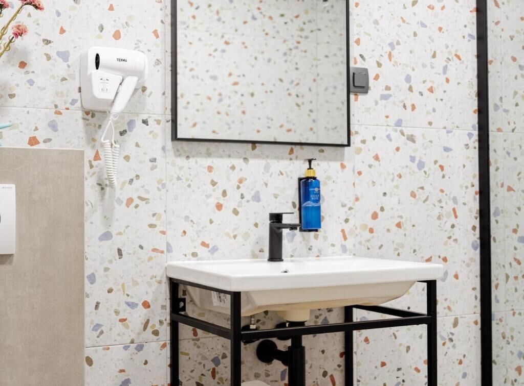Un bagno con lavandino bianco, uno specchio, un asciugamani ad aria e un dispenser di sapone.