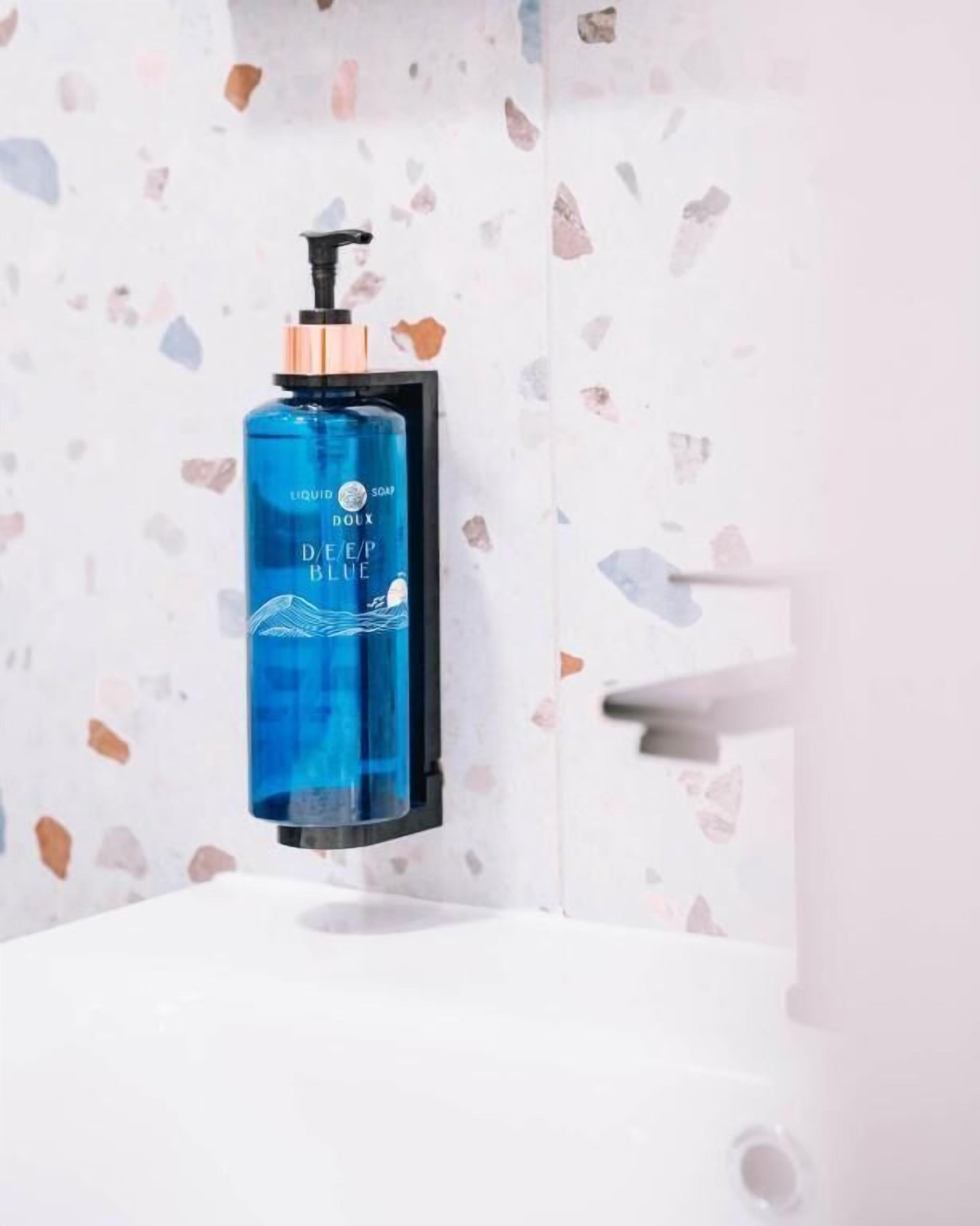 A bathroom with a blue soap dispenser mounted on a wall with a terrazzo tile backsplash.