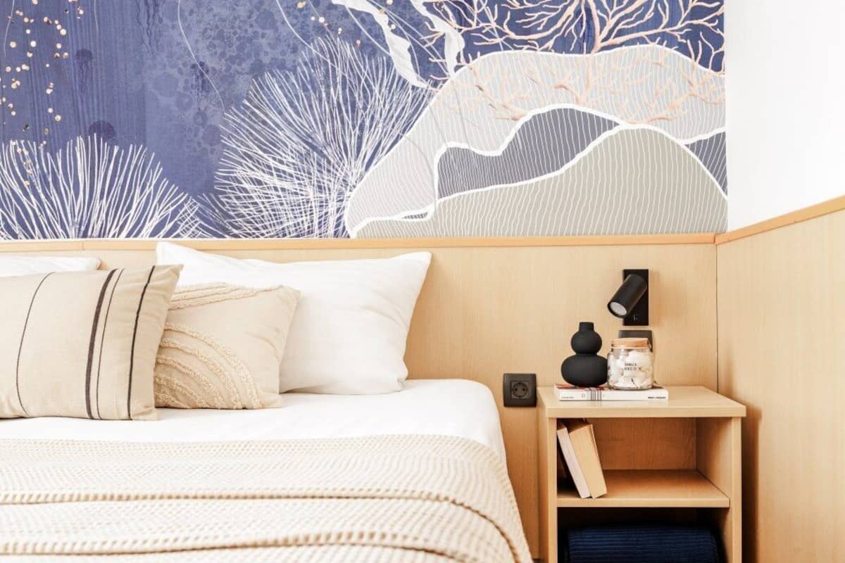 Ein Schlafzimmer mit Bett, Kissen, einem Nachttisch und einer Wandmalerei.