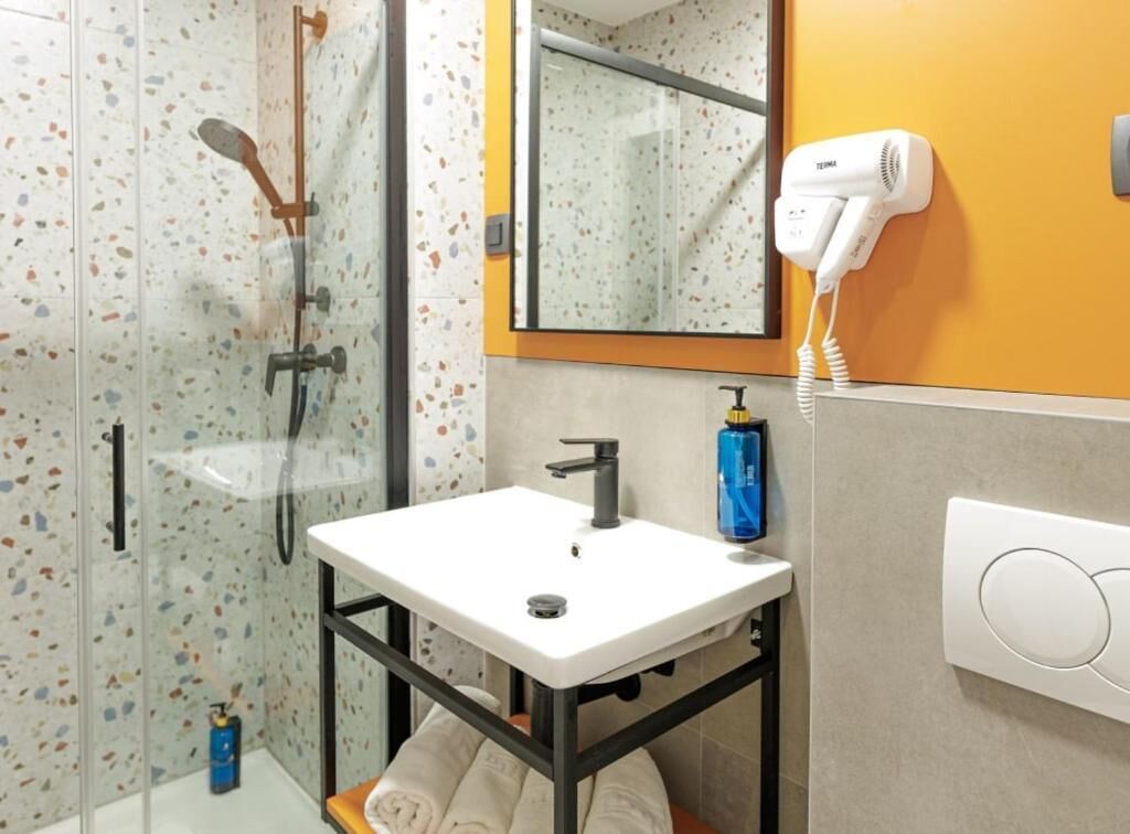 Une salle de bain avec une douche à parois de verre, un lavabo blanc, un sèche-cheveux et un porte-serviettes.