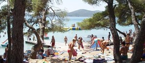 A beach scene with people sunbathing and swimming, surrounded by trees and a clear view of the sea. - Hotel Bolero (Biograd na Moru)