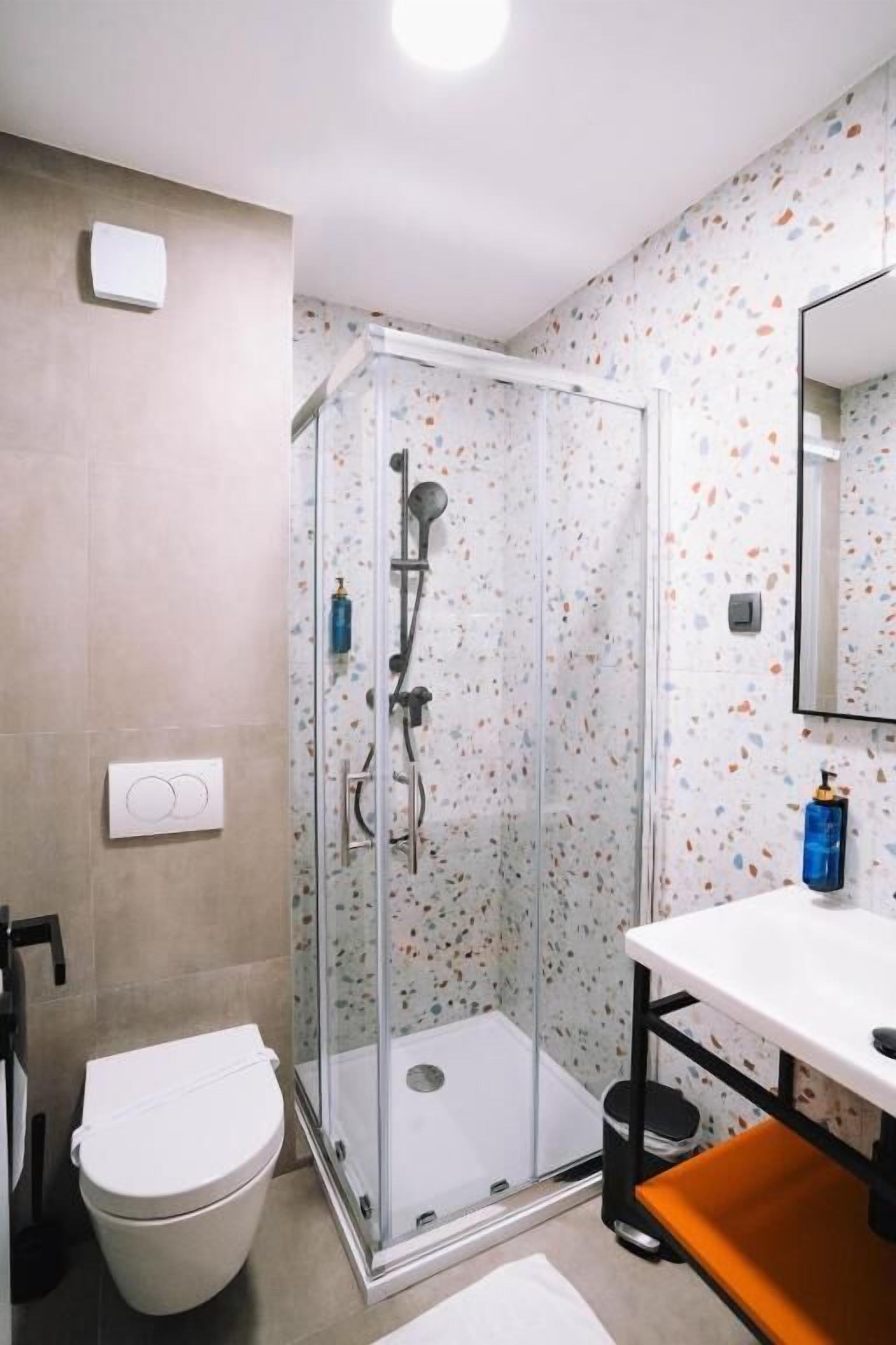 A bathroom with a glass-enclosed shower, a white toilet, and a white sink with a mirror above it.