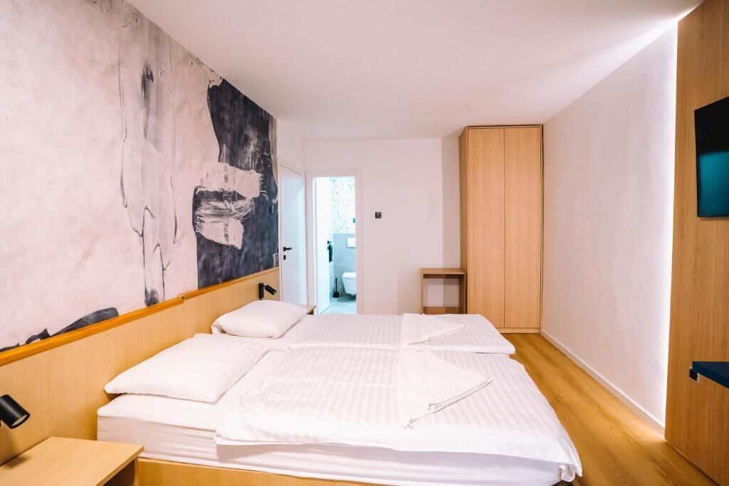 Ein modernes Schlafzimmer mit einem großen abstrakten Gemälde an der Wand, einem Holzschrank und einem ordentlich bezogenen Bett.