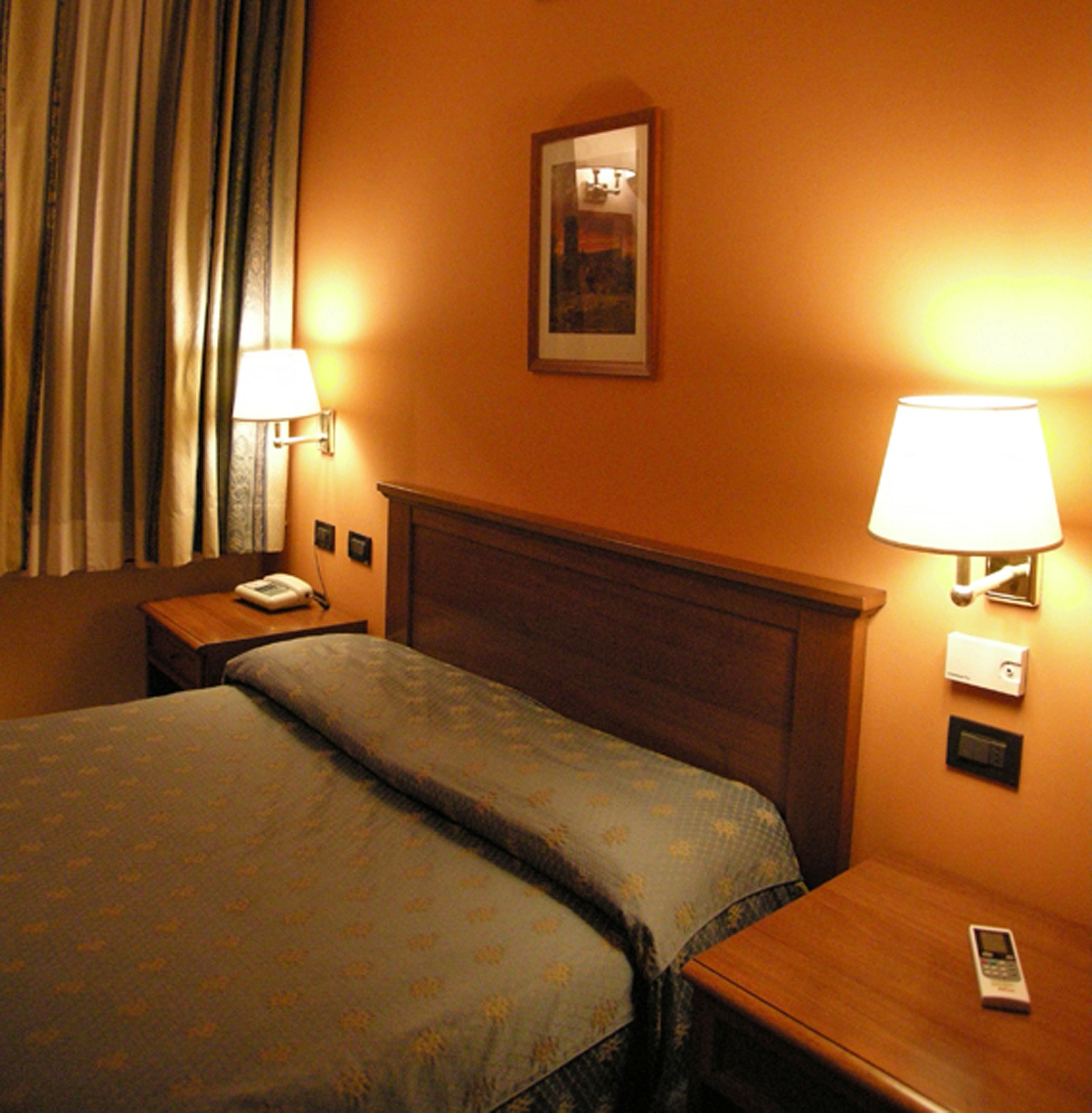 A hotel room with a bed, two bedside tables, a lamp on each table, a phone on one table, and a picture on the wall.