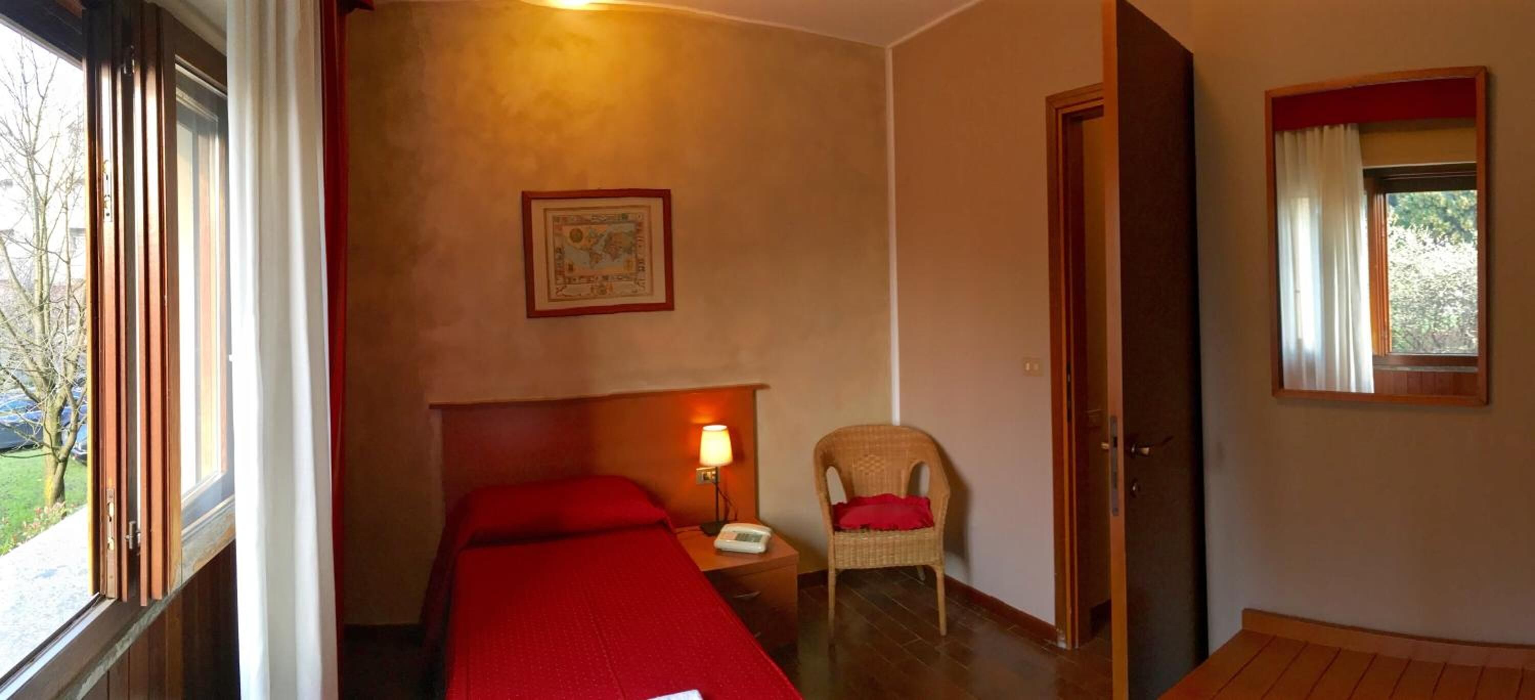 Habitación de hotel con cama, una silla, mesita de noche, lámpara y un cuadro en la pared.