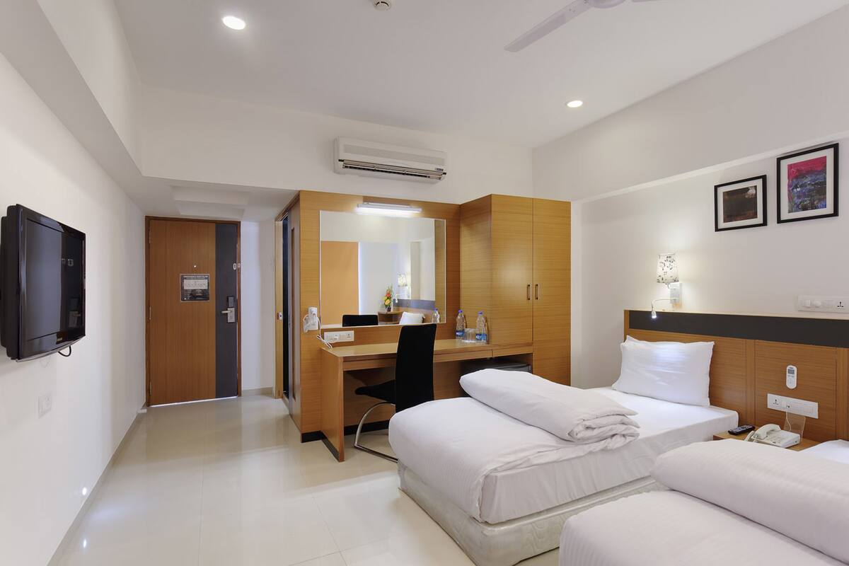 A hotel room with a bed, bedside table, desk, chair, and a television.