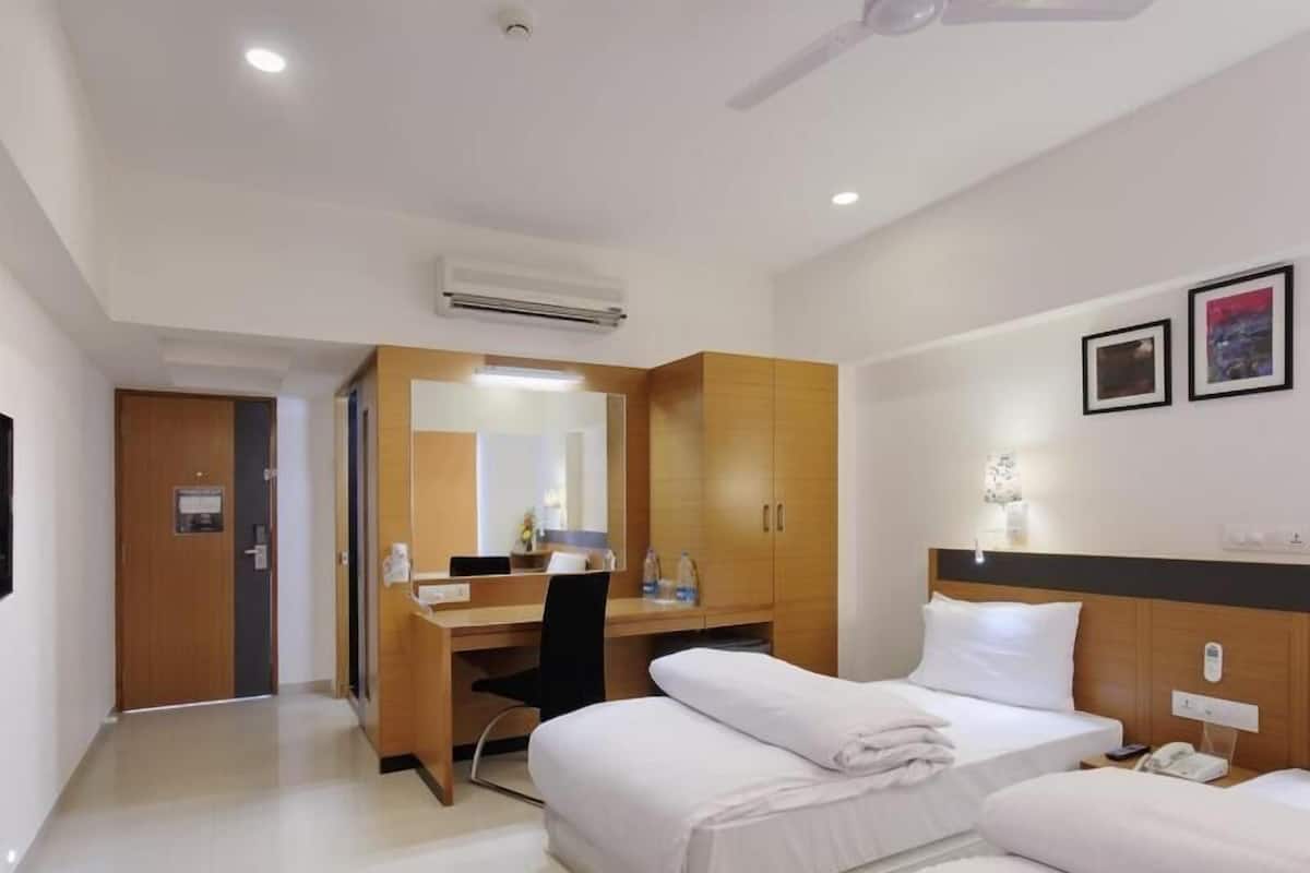 A hotel room with a bed, a desk, a chair, an air conditioning unit, and a ceiling fan.