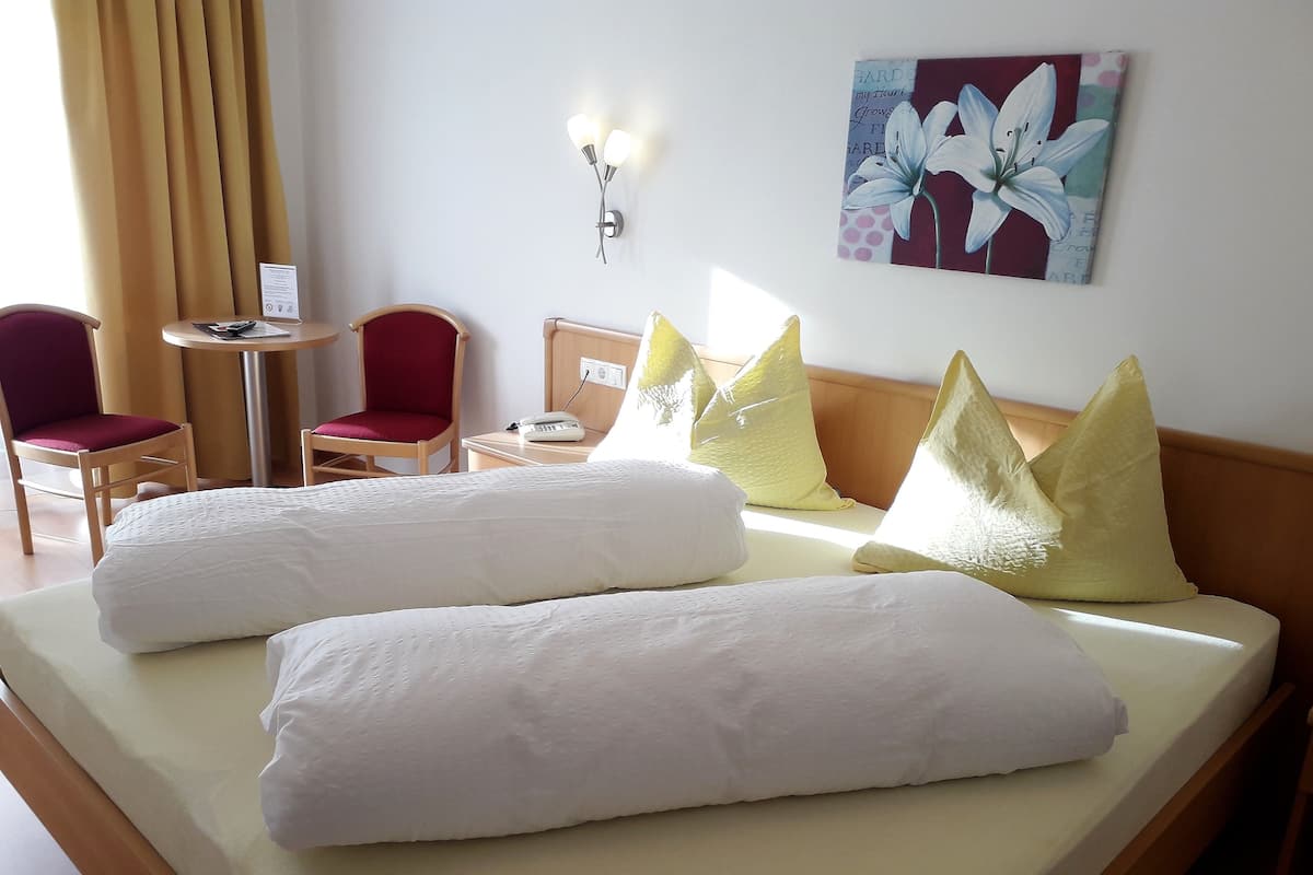A hotel room with a bed, two chairs, a small table, and a wall-mounted light fixture.