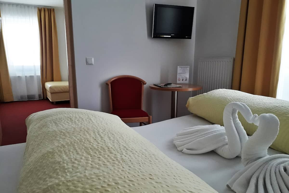 A hotel room with two beds, a television on the wall, a small table, and a chair.
