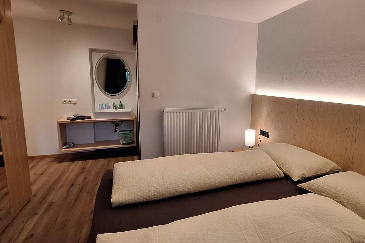 A room with two beds, a wooden headboard, a mirror, a small shelf with toiletries, and a radiator.
