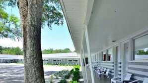 A covered outdoor seating area with white chairs, a tree, and a building in the background. - Sun Plaza Motel (Silver Springs)