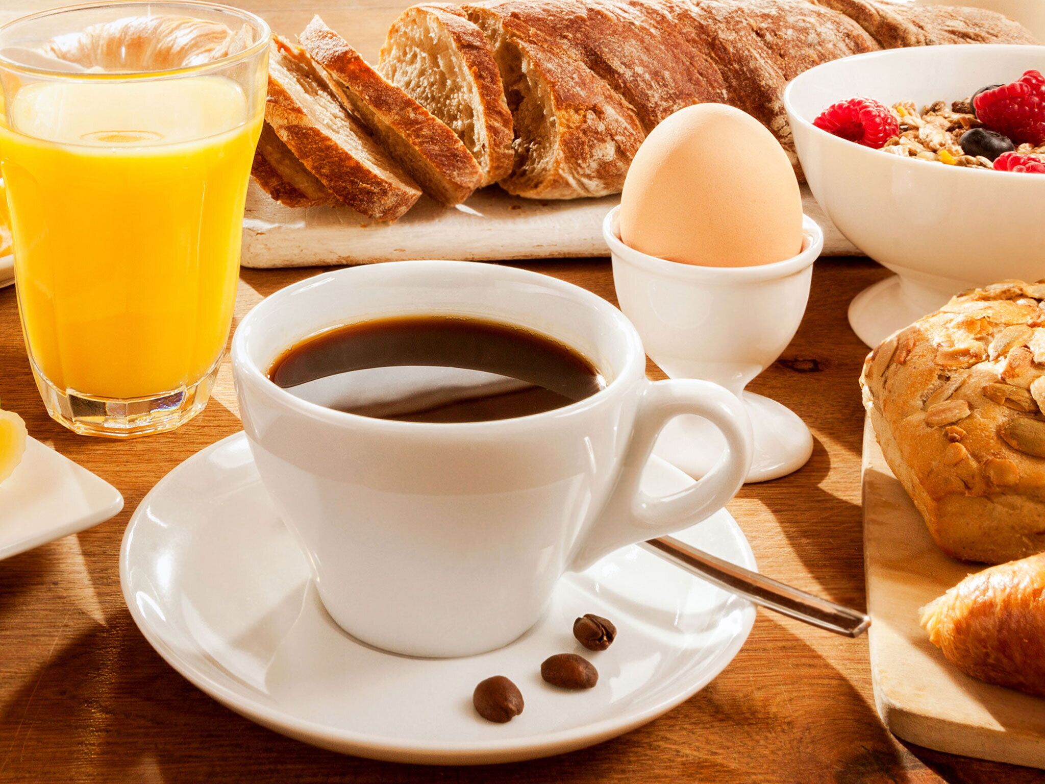 Impostazione per la colazione con una tazza di caffè, un bicchiere di succo d'arancia, un croissant, una ciotola di cereali con frutti di bosco e un pasticcino su un tavolo di legno.