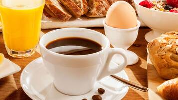 Impostazione per la colazione con una tazza di caffè, un bicchiere di succo d'arancia, un croissant, una ciotola di cereali con frutti di bosco e un pasticcino su un tavolo di legno.