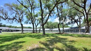 A grassy area with trees and a row of buildings with a flat roof. - Sun Plaza Motel (Silver Springs)