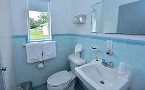 A bathroom with a toilet, sink, and window. - Sun Plaza Motel (Silver Springs)