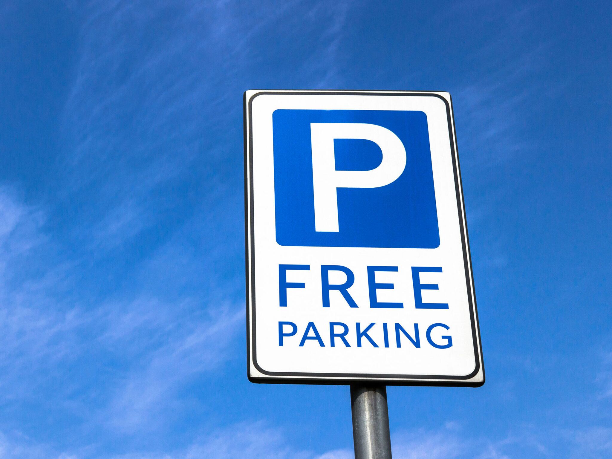 Un panneau de signalisation indiquant un parking, avec un « P » bleu et les mots « PARKING GRATUIT » sur un fond de ciel bleu clair.