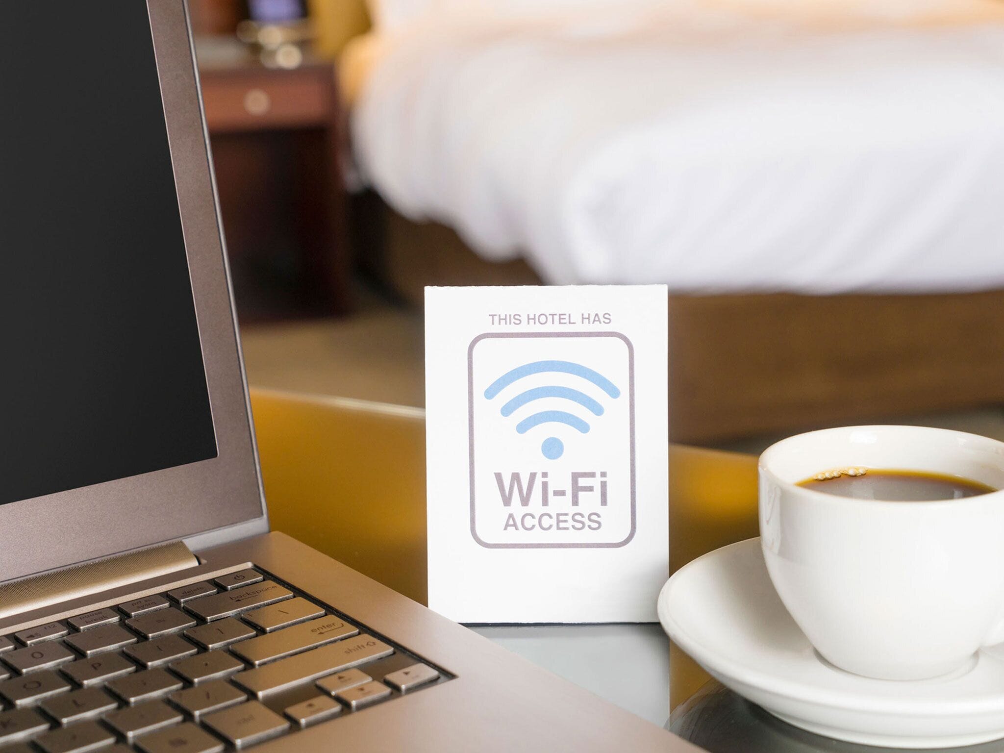 A laptop, a Wi-Fi access sign, and a cup of coffee on a hotel table.
