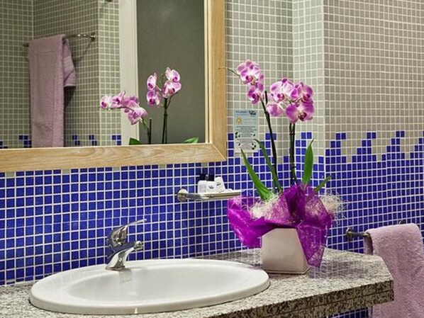 A bathroom with a sink, mirror, and purple orchids.