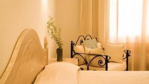 Una cama con cabecera, una mesita de noche con un jarrón de flores y una ventana con cortinas.