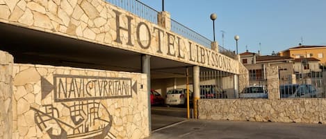 A stone facade with a sign reading "HOTEL LIBYSSONIS" and a parking garage entrance.