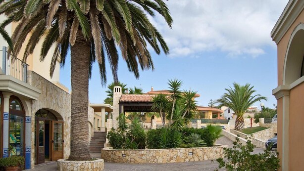 Un patio con paredes de piedra, palmeras y un edificio de techo a tejas.