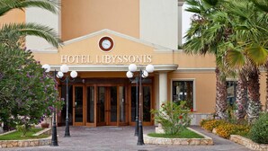 La entrada del Hotel Libyssonis, con un acceso central, puertas de cristal y un reloj encima.