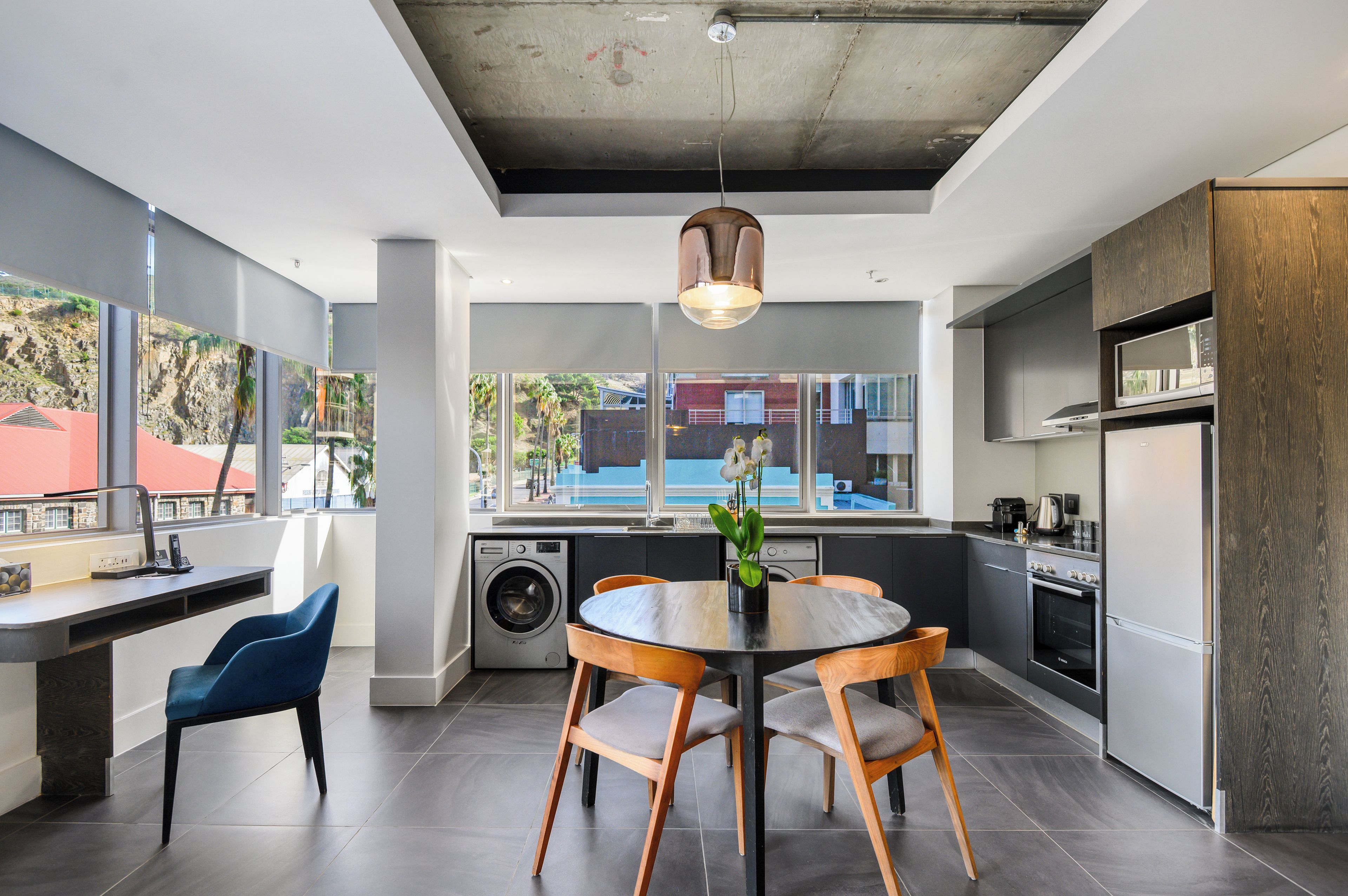 Een moderne keuken met een eethoek, grote ramen en uitzicht op buiten.