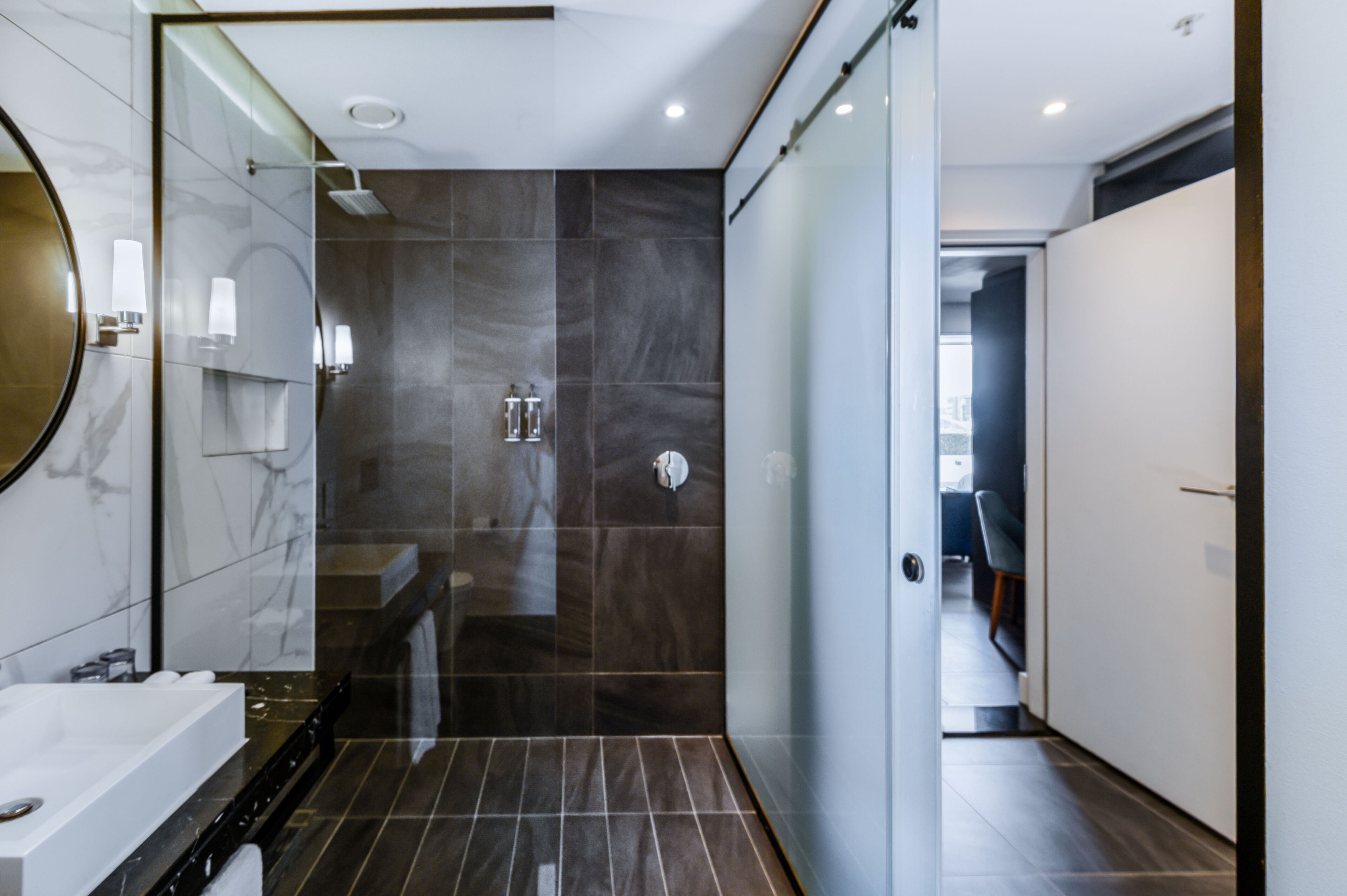 Un baño moderno con un espejo grande, una bañera, una ducha y un vestidor con puertas de vidrio.