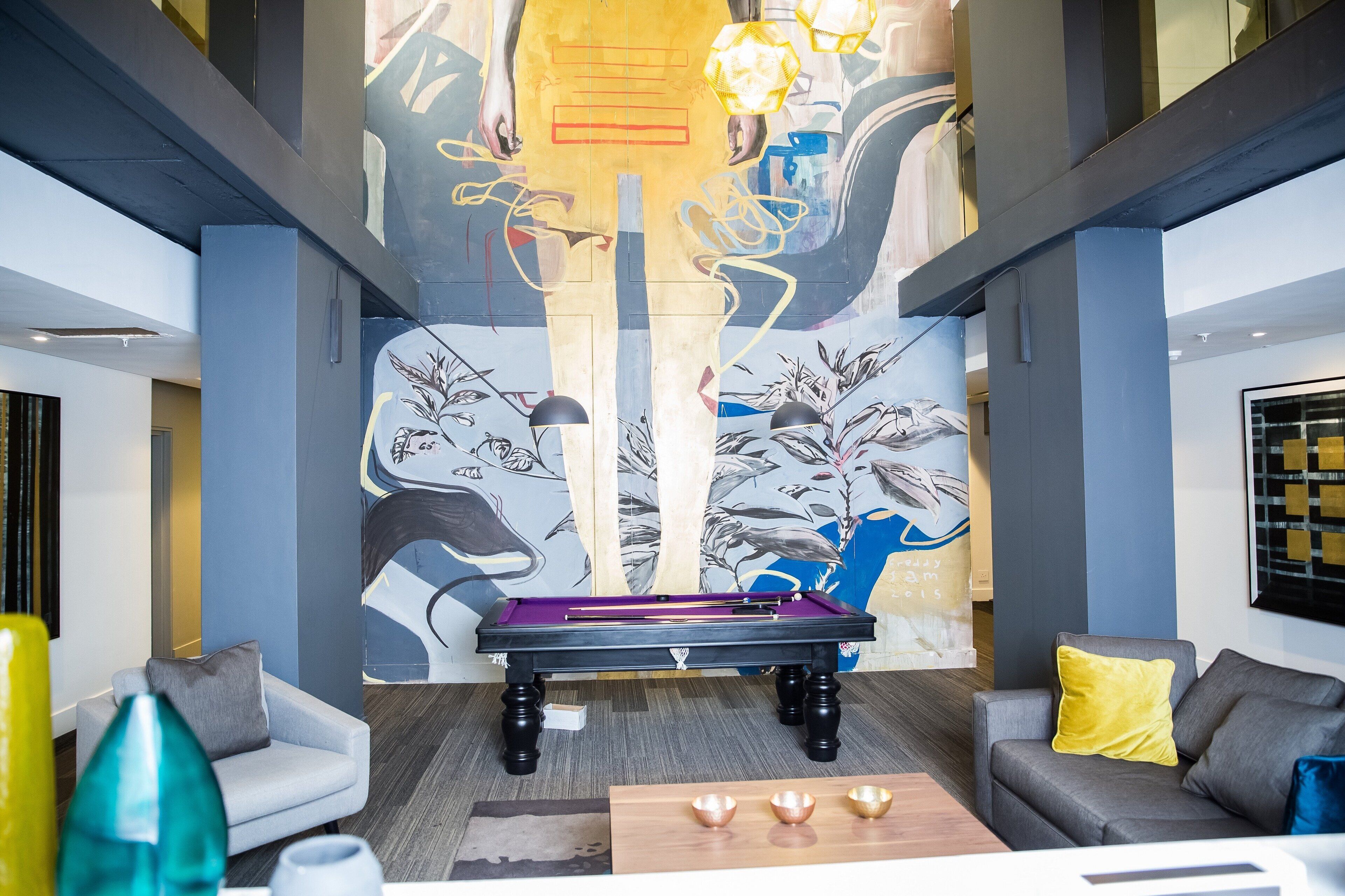 Uma mesa de bilhar em uma sala moderna, com arte abstrata nas paredes e dois sofás.