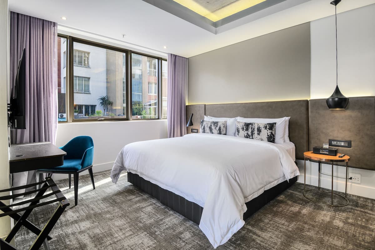 A modern hotel room with a large bed, a desk, a chair, and a view of the city.