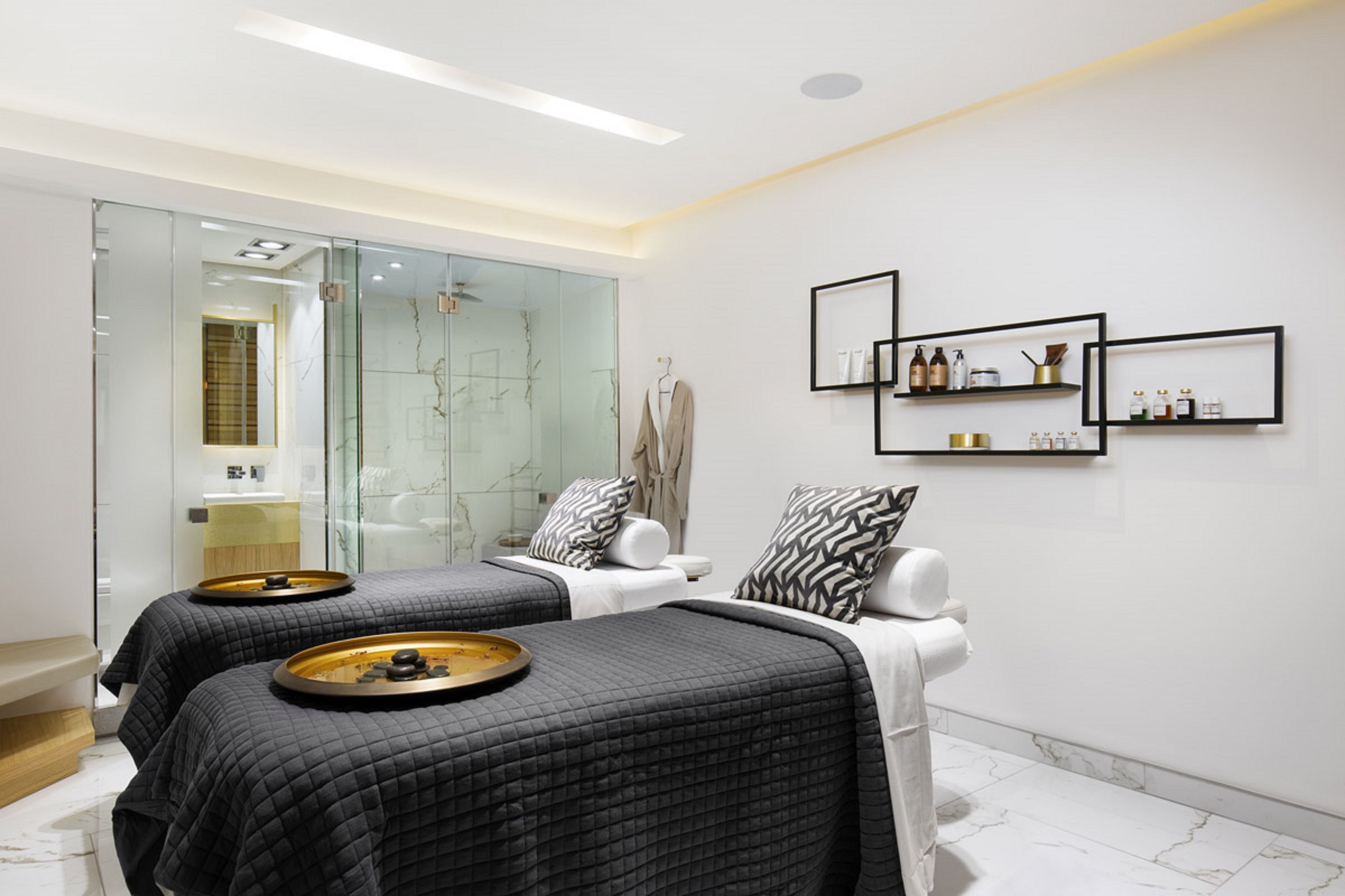 A modern spa room with two beds, a glass shower area, and shelves with toiletries.
