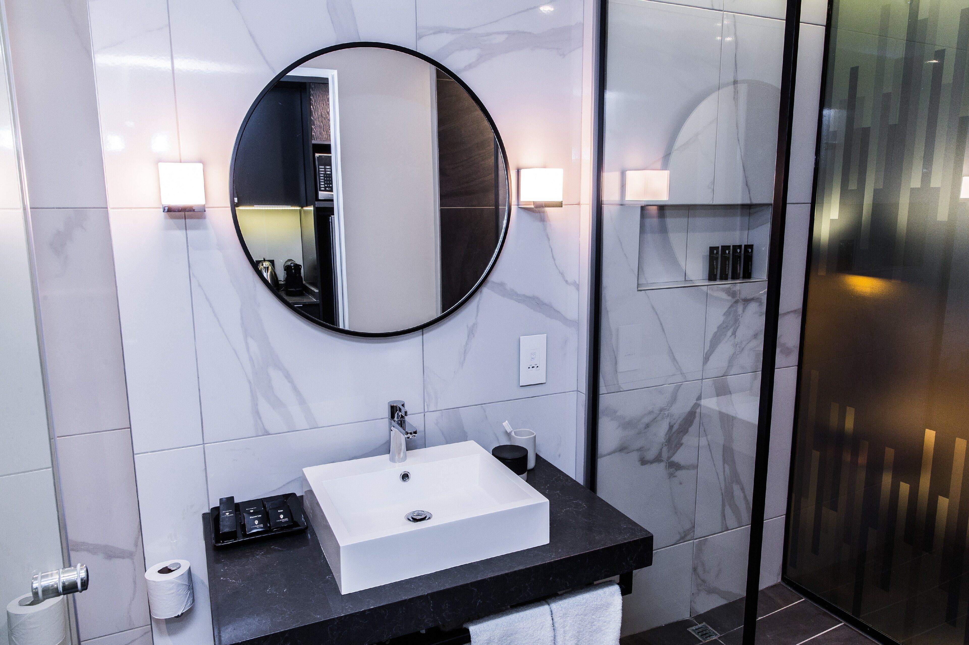 A modern bathroom with a white sink, black countertop, and a round mirror.